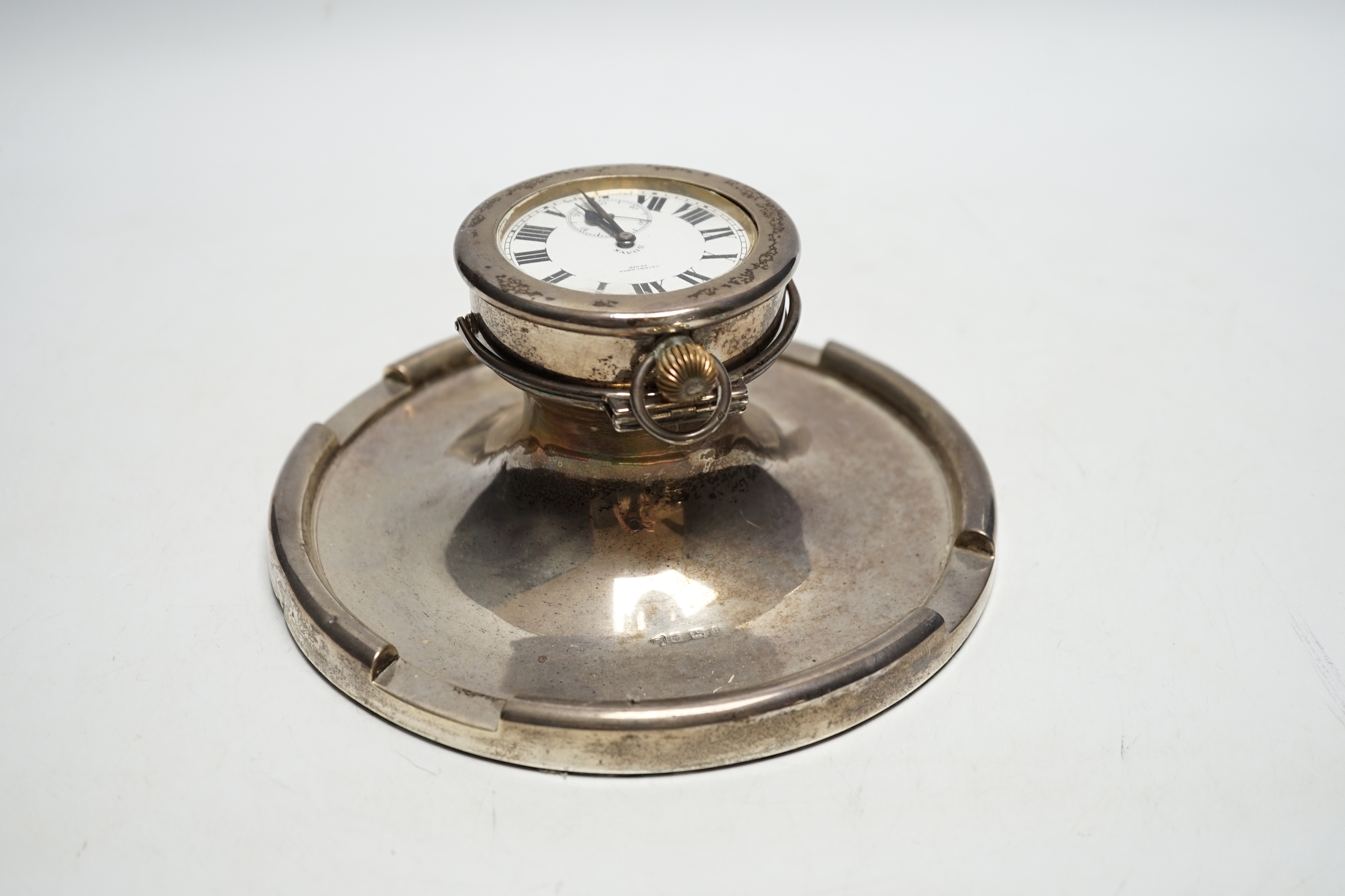 A George V silver mounted combination inkwell/pocket watch holder, Birmingham, 1926, containing an eight day pocket watch, Cairncross, Perth, base diameter 17.7cm.